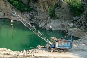 Mining in the granite quarry. Working mining machine - old crane. Mining industry. photo