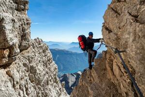 Male mountain climber on a Via Ferrata in breathtaking landscape of Dolomites Mountains in Italy. Travel adventure concept. photo