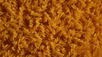 Uncooked Fusilli Pasta - Top View, Low Key Light. Fat and Unhealthy Food. Dry Spiral Macaroni, Slowly Rotating Background. Italian Culture and Cuisine. Raw Golden Pasta Pattern. Right Rotation video