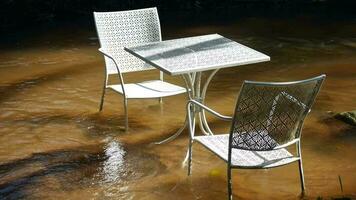 Stream of water are flowing through the tables and chairs, Beautiful white chairs and tables sit in the middle of a natural stream, A table set for tea drinking in the garden video