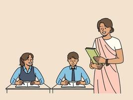 Indian woman teacher works in primary school, standing near children sitting at desks in classroom. Girl teacher from india, makes career in education and gives kids new knowledge. vector