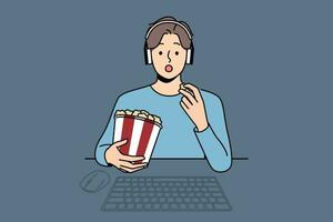 Man with package of popcorn watches movie sitting at table with computer and looks at screen intrigued. Funny guy in headphones is relaxing watching new movie blockbuster or popular tv series vector