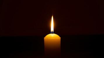 A single burning candle flame or light glowing on a big yellow candle isolated on red or dark background on table in church for Christmas, funeral or memorial service photo