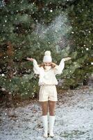 Smiling stylish young woman plays with snow in spruce forest. Snowy weather. High quality photo