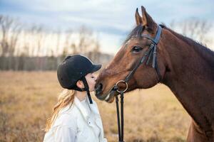 Beautiful professional female jockey kissing horse. Friendship with horse concept. High quality photo