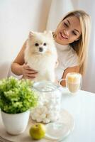 Beautiful young woman with Pomeranian spitz dog and cup of coffee in cozy cafe. High quality photo