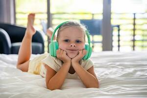 pequeño niña escuchando música utilizando verde niños auriculares auriculares en hogar cama. alto calidad foto