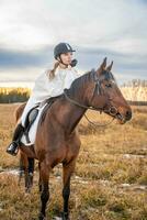 Beautiful blond professional female jockey riding a horse in field. Friendship with horse. High quality photo