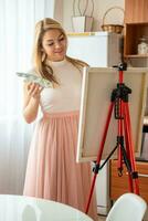 hermosa joven rubia mujer artista con paleta y cepillo pintura resumen rosado imagen en lona a hogar. Arte y creatividad concepto. alto calidad foto