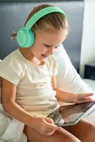 Cute little girl in headphones using digital tablet while listening to music or playing game in home bed. High quality photo