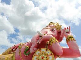 Bright pink painted Ganesha concrete statue recline posture and clouds on sky background, Thailand. photo