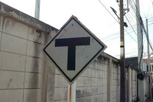 Black junction sign on white square shape board on pole beside dirty concrete wall. photo