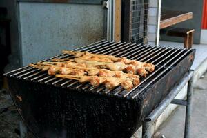 Cooked chicken's wings clamped bamboo stick on metal grate of charcoal stove, wings marinate sauce before coolking, Thailand. photo