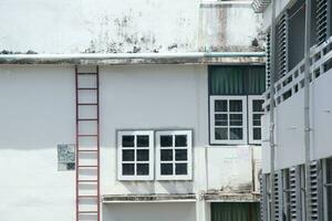 blanco ventana cerrado con tinte en blanco pintado pared de antiguo y sucio, rayado edificio. rojo acero escalera junto a con vaso bloquear en muro, Bankok en tailandia foto