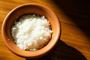 Rice in clay pot on wooden table with sun light. photo