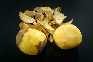 Raw peeled potatoes and potato peelings on black background photo