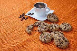 Chocolate chip cookies and cup of coffee shot on jute colored cloth. photo