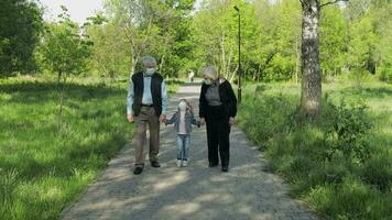 Old grandparents with granddaughter in medical masks walk in park. Coronavirus video