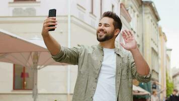 Young man blogger taking selfie on smartphone video call online with subscribers in city street