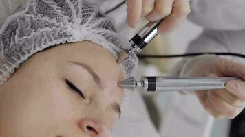 Middle-aged woman receiving micro currents facial forehead skin treatment from beautician in salon video