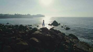 un niña soportes en el rocas a puesta de sol video