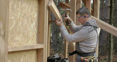 Man worker building wooden frame house. Carpenter hammering nail into wooden joist, using hammer. Carpentry concept. video