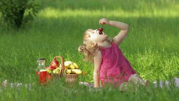 Weekend at picnic. Lovely caucasian child girl on green grass meadow eating merry, cherry video