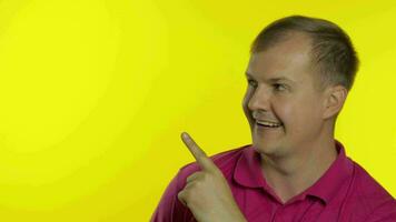 Portrait of young man posing in pink t-shirt. Happy smiling guy pointing at something with hand video