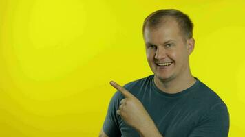 Portrait of young man posing in green t-shirt. Happy smiling guy pointing at something with hand video