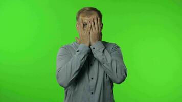 Shy guy scared to watch. Man covering eyes with hands and looking cautiously curious at camera video