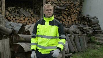 Lumberjack in reflective jacket. Man woodcutter show thumb up. Sawn logs, firewood background video