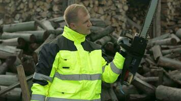 Lumberjack worker. Man woodcutter holds big axe and electric chainsaw on his hands. Firewood video