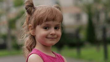 Little child girl against the blurred city street background. Cheerful, positive emotions, smile video