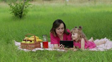 Family weekend picnic. Daughter child girl with mother study lessons on tablet. Distance education video