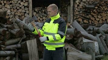 Lumberjack in reflective jacket. Man woodcutter with small axe. Sawn logs, firewood background video