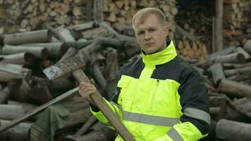 Holzfäller im reflektierend Jacke. Mann Holzfäller mit groß Axt. gesägt Protokolle, Brennholz Hintergrund video