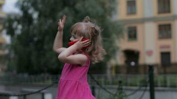 enfant fille parlant par téléphone intelligent en plein air. enfant dans rose robe parlant par mobile téléphone sur ville rue video