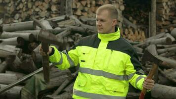Lumberjack in reflective jacket. Man woodcutter holds small and big axes on his hands. Firewood video
