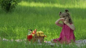 Weekend at picnic. Lovely caucasian child girl on green grass meadow eating merry, cherry video