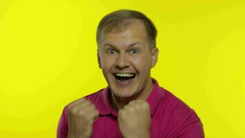 porträtt av ung caucasian man Framställ i rosa t-shirt. nöjd stilig kille firar, vinner video