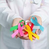 World cancer day, February 4. Doctor holding blue, red, green, white, pink, blue and yellow ribbons for supporting people living and illness. Healthcare and Autism awareness day concept photo