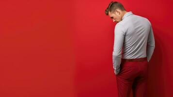 ai generado un hombre en rojo pantalones y blanco camisa soportes contemplativamente en contra un vibrante rojo fondo, exudando un sentido de introspección. foto