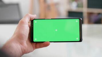 Man hand holding the smartphone horizontally with green screen on watching ideos video