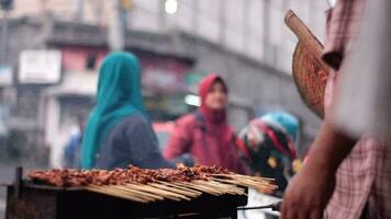 kyckling satay över traditionell träkol brand. de satay brännskador med rök och ett aptitlig utseende. händer matlagning satay på de grill. människor är redan köa. video