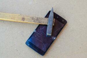 Hammer and smartphone. The screen of the smartphone, a broken ha photo