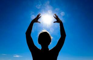 Silhouette of a girl against the background of the sun and blue sky. Hands are raised up to the sun photo