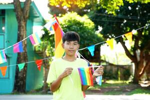 Asian boy holds a rainbow flag in front of a house decorated with rainbow flags during Pride Month to show LGBT pride and identity. Soft and selective focus. photo