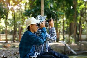 Asian boys use binoculars to look at birds in a community forest own. The concept of learning from learning sources outside the school. Focus on the first child. photo