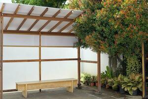 A model of a Japanese bus waiting seat.it is a photo corner at a Japanese-style coffee shop. The surrounding area is decorated with many types of ornamental plants. Soft and selective focus.