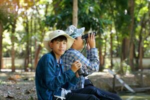 Asian boys use binoculars to look at birds in a community forest own. The concept of learning from learning sources outside the school. Focus on the first child. photo